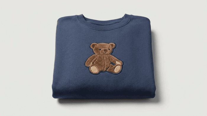 A folded navy sweatshirt with an embroidered teddy bear patch